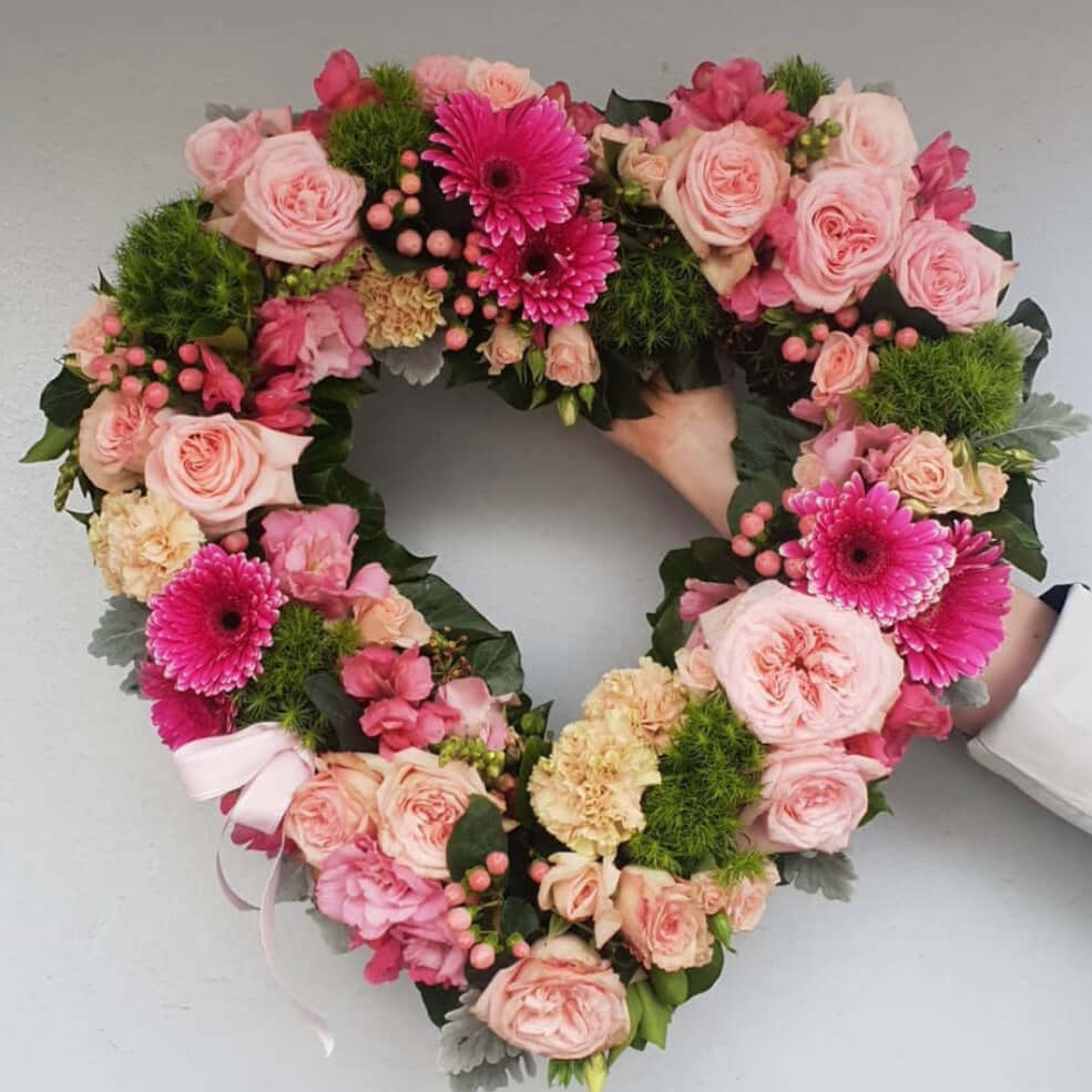 Heart shaped sympathy wreath adorned with pink roses, gerberas, and seasonal blooms by Berwick Flowers.