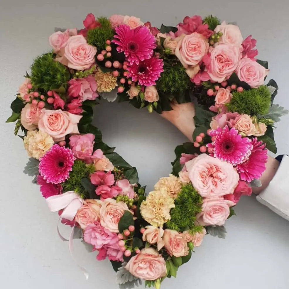 Heart shaped sympathy wreath adorned with pink roses, gerberas, and seasonal blooms by Berwick Flowers.