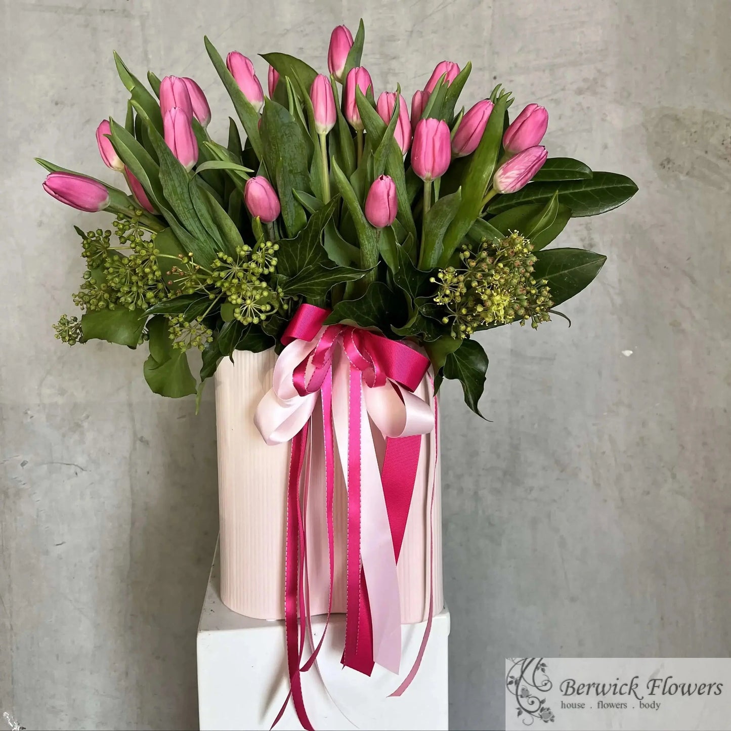 Bouquet of pink tulips in a vase with pink ribbons against a gray background