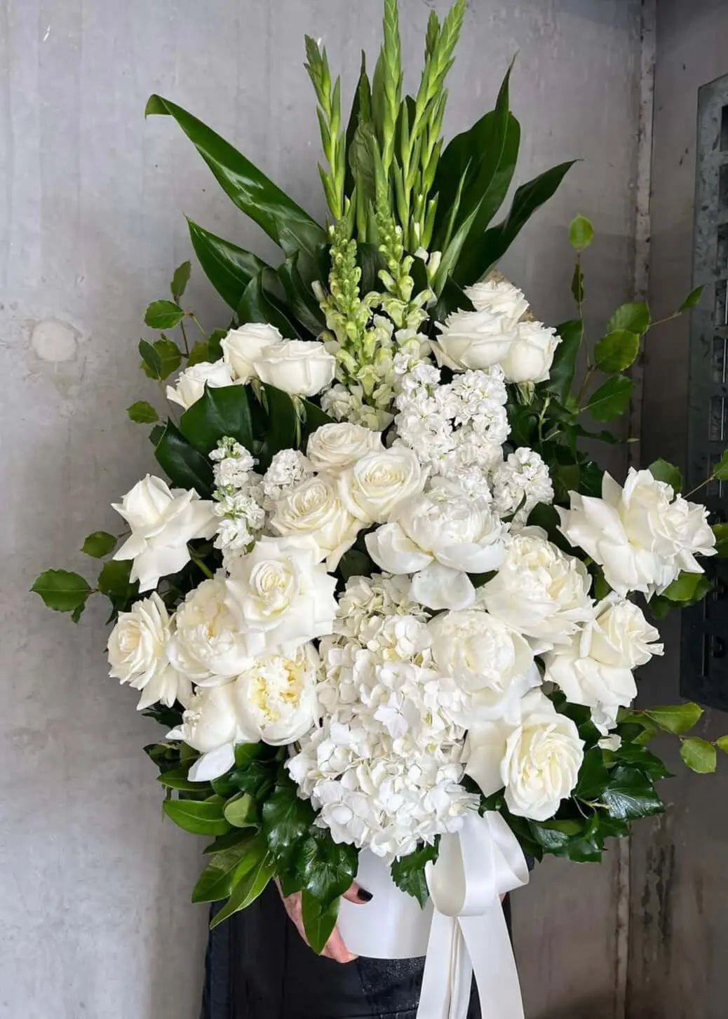 Classic white standing sympathy arrangement with white roses, hydrangeas, and greenery.