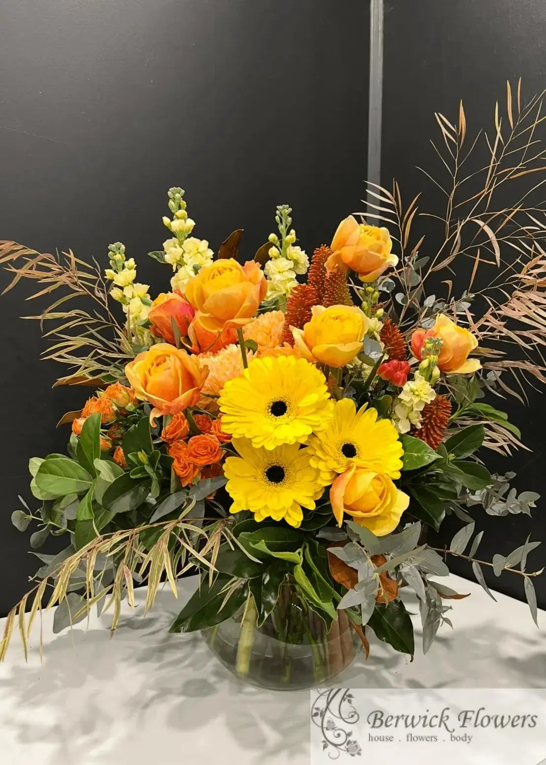 Bouquet of yellow and orange flowers in a clear vase on a dark background