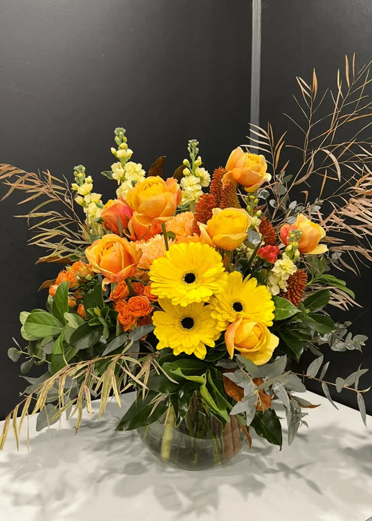 Bouquet of yellow and orange flowers in a clear vase on a dark background