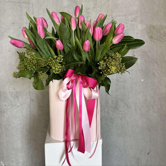 Mother's Day pink tulip flowers in a pink vase with ribbons and green accents.