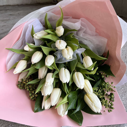white tulip bouquet for Mother's Day in soft pink wrapping with greenery accents.