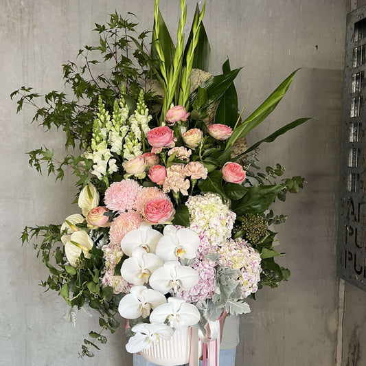 Mother's Day flower arrangement featuring pink roses, orchids, and lush greenery in a decorative vase.