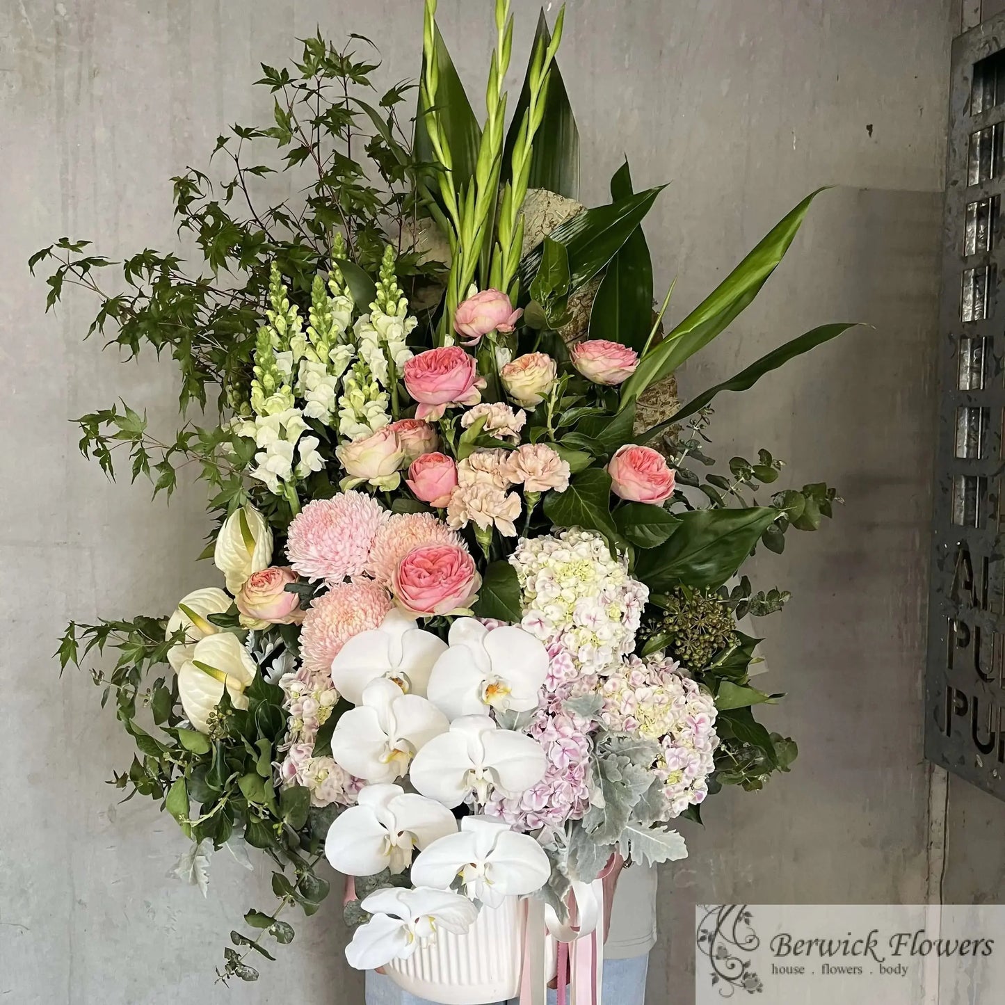 Bouquet of flowers with pink and white flowers in a vase against a concrete wall.