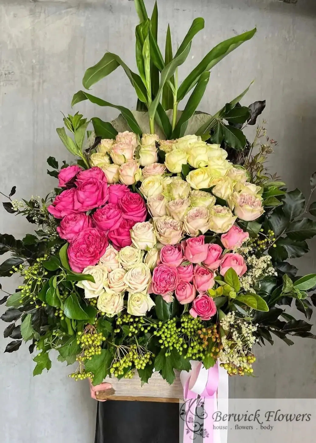 Bouquet of pink and white flowers with greenery on a stand against a gray background